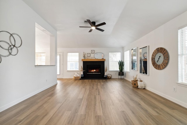 unfurnished living room with a lit fireplace, baseboards, ceiling fan, and wood finished floors