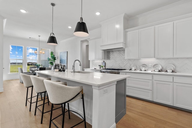 kitchen with a center island with sink, a sink, light countertops, crown molding, and backsplash