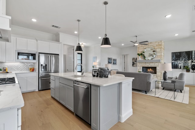 kitchen with light wood finished floors, tasteful backsplash, appliances with stainless steel finishes, a stone fireplace, and a sink