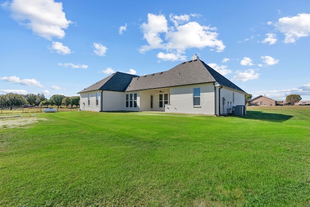 back of house featuring brick siding, a shingled roof, a lawn, central AC unit, and fence