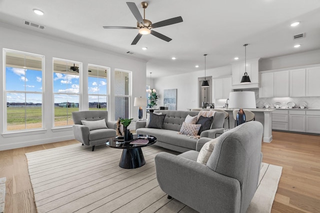 living room with light wood-type flooring, visible vents, crown molding, and recessed lighting