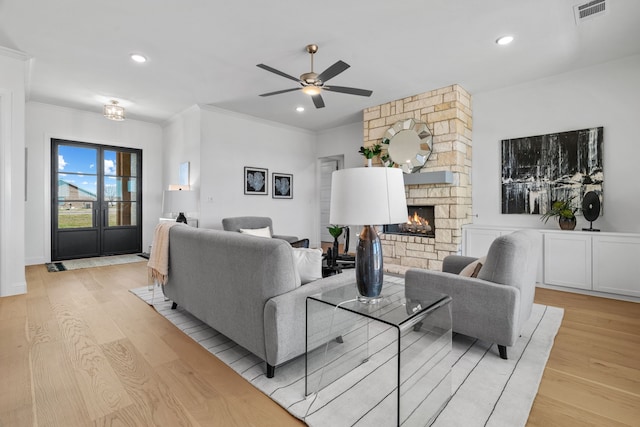 living area featuring visible vents, crown molding, a stone fireplace, light wood-type flooring, and recessed lighting