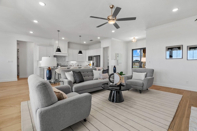 living area with ceiling fan, recessed lighting, baseboards, light wood-style floors, and ornamental molding