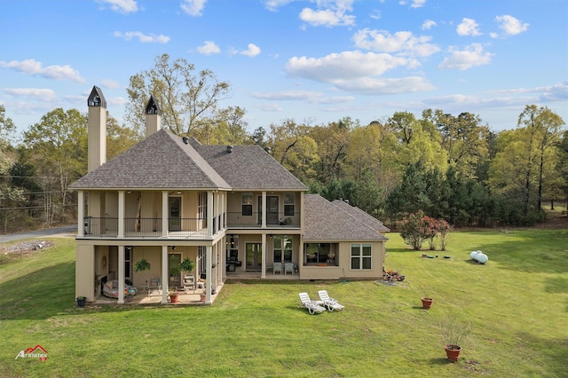 back of property with a shingled roof, a patio area, a yard, and stucco siding