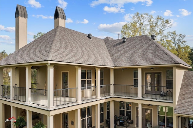 back of house featuring a shingled roof, a chimney, a balcony, and stucco siding