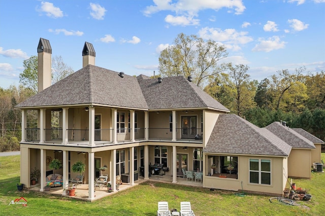 rear view of house with a yard, a patio, stucco siding, a shingled roof, and a balcony