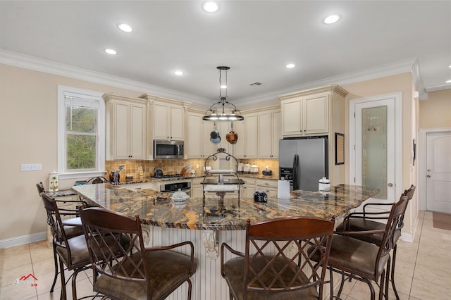 kitchen featuring ornamental molding, dark stone countertops, cream cabinets, stainless steel appliances, and backsplash