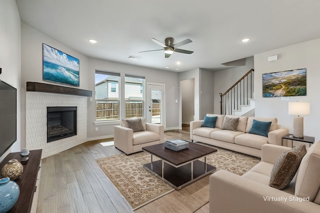 living room featuring baseboards, wood finished floors, stairs, a brick fireplace, and recessed lighting