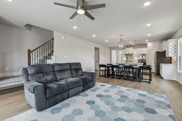 living area with recessed lighting, baseboards, light wood-style flooring, stairway, and ceiling fan with notable chandelier