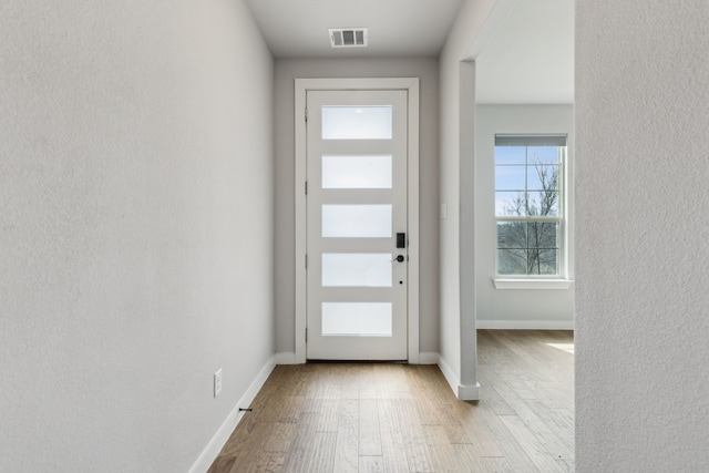 doorway to outside with a textured wall, wood finished floors, visible vents, and baseboards