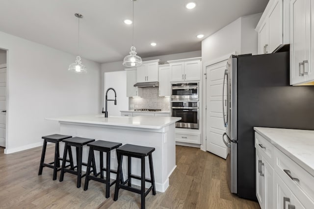 kitchen with a breakfast bar, stainless steel appliances, decorative backsplash, a sink, and under cabinet range hood