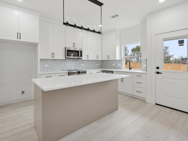 5809 Black Pine Cir, Granbury, TX 76048 - kitchen featuring appliances with stainless steel finishes, a kitchen island, decorative backsplash, light countertops, and white cabinets