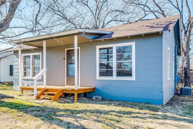 exterior space featuring central AC unit, roof with shingles, and concrete block siding