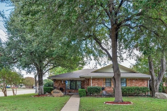 ranch-style house featuring a shingled roof, a front lawn, and brick siding