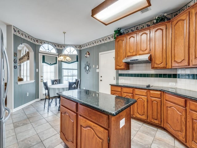 kitchen featuring under cabinet range hood, a kitchen island, brown cabinetry, and an inviting chandelier