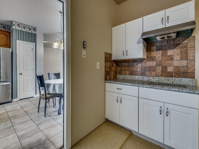 kitchen with under cabinet range hood, tasteful backsplash, freestanding refrigerator, white cabinets, and stone counters