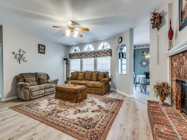 living room featuring a brick fireplace, light wood-style flooring, baseboards, and ceiling fan