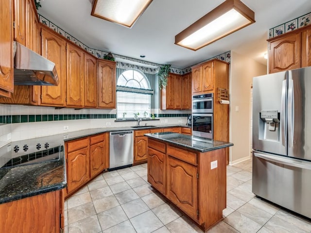 kitchen with brown cabinets, a sink, stainless steel appliances, under cabinet range hood, and tasteful backsplash