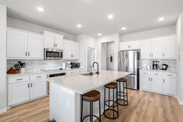 kitchen featuring a kitchen island with sink, a sink, a kitchen breakfast bar, stainless steel appliances, and light wood finished floors