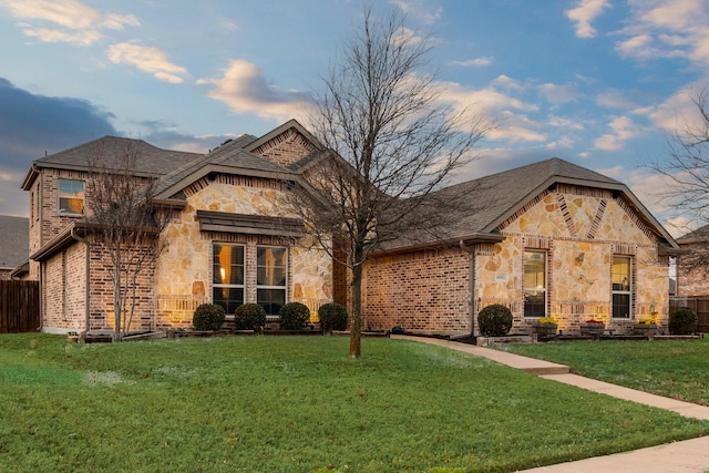 french country home with a front yard, stone siding, and fence