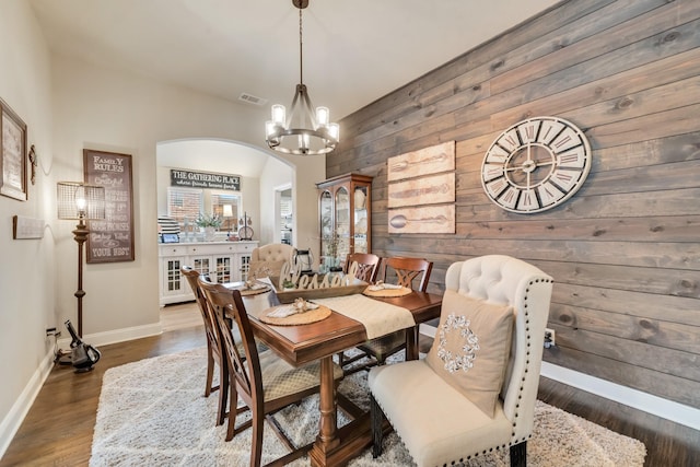 dining area featuring wooden walls, baseboards, arched walkways, wood finished floors, and a notable chandelier