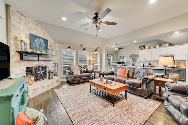 living room with a fireplace, vaulted ceiling, visible vents, and wood finished floors