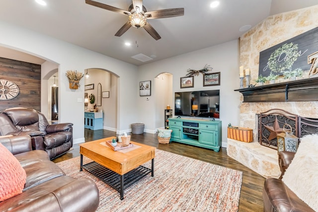 living area with arched walkways, ceiling fan, a stone fireplace, recessed lighting, and dark wood finished floors