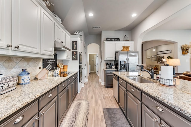 kitchen featuring arched walkways, appliances with stainless steel finishes, white cabinets, a sink, and under cabinet range hood