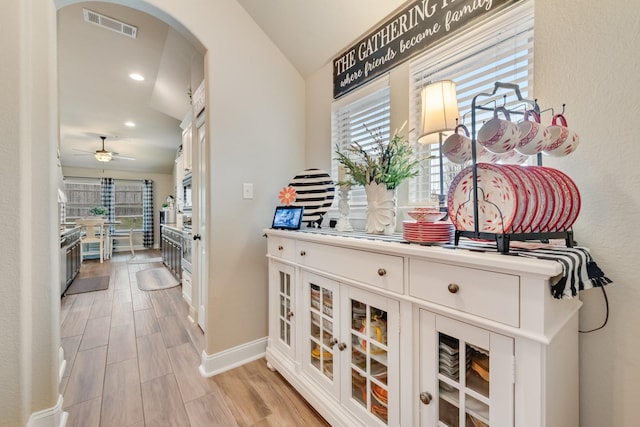 corridor featuring arched walkways, recessed lighting, visible vents, light wood-type flooring, and baseboards