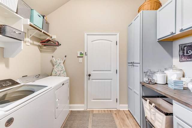 clothes washing area featuring baseboards, washing machine and clothes dryer, cabinet space, and light wood-style floors