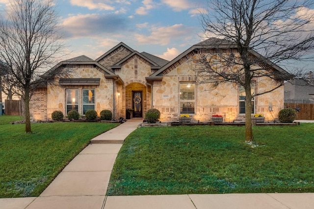 french country home with stone siding, a front yard, and fence