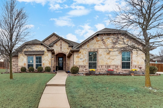 french country style house with fence, a front yard, and stone siding