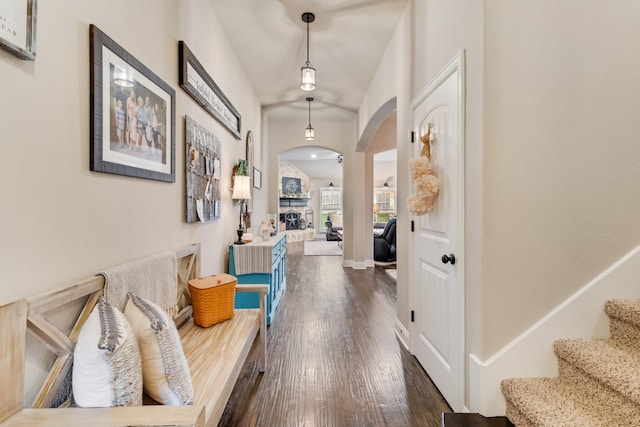 hall featuring arched walkways, dark wood-style flooring, and stairs