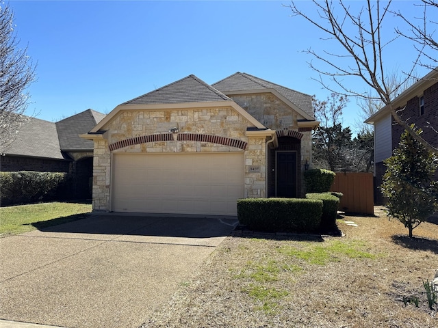 french provincial home featuring a garage, stone siding, and concrete driveway