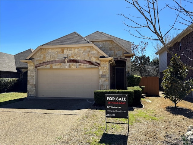 french country style house with driveway, stone siding, and an attached garage