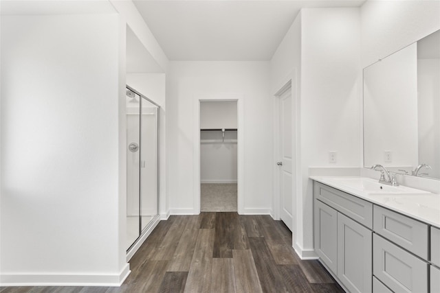 bathroom with baseboards, wood finished floors, a walk in closet, vanity, and a shower stall