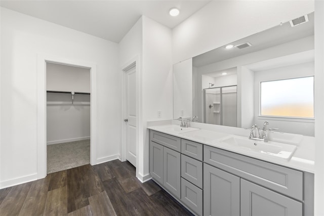 bathroom featuring double vanity, a sink, a shower stall, wood finished floors, and baseboards