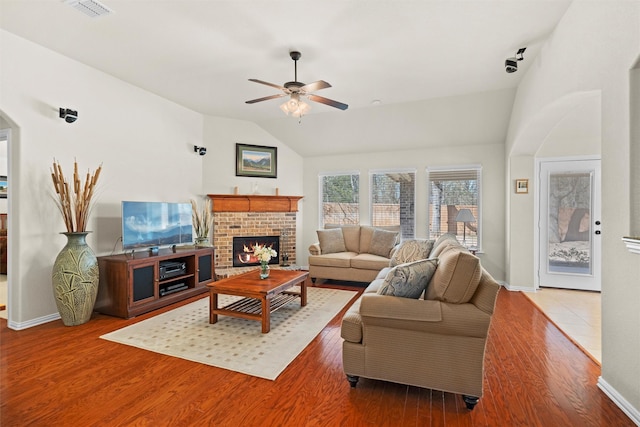 living room featuring lofted ceiling, a fireplace, wood finished floors, visible vents, and a ceiling fan