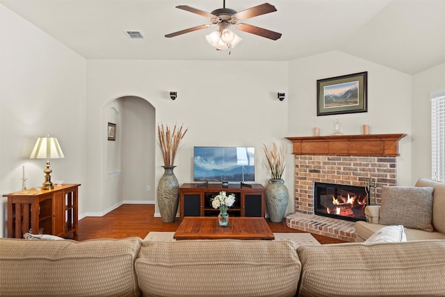 living room featuring a fireplace, lofted ceiling, visible vents, ceiling fan, and wood finished floors