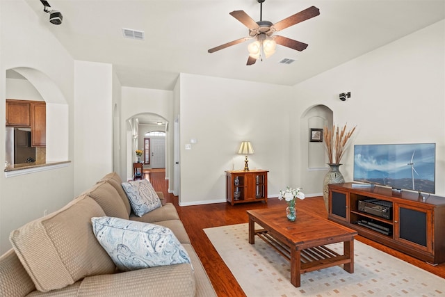 living area featuring a ceiling fan, arched walkways, visible vents, and wood finished floors