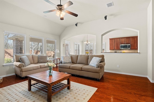 living room featuring lofted ceiling, visible vents, wood finished floors, baseboards, and ceiling fan with notable chandelier