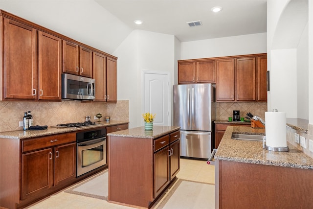 kitchen with stainless steel appliances, a kitchen island, visible vents, and light stone countertops