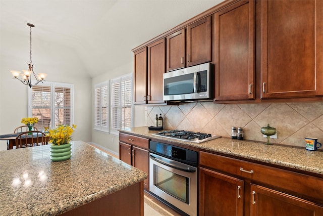 kitchen featuring light stone counters, hanging light fixtures, decorative backsplash, appliances with stainless steel finishes, and vaulted ceiling