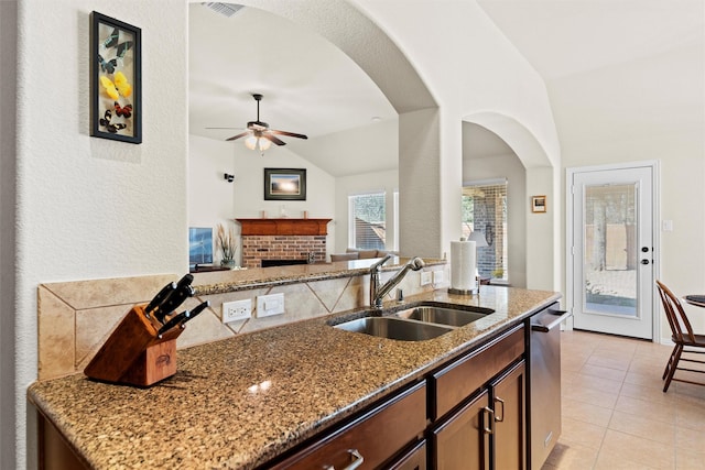 kitchen featuring stone countertops, light tile patterned flooring, a sink, a brick fireplace, and dishwasher