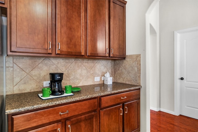 kitchen with arched walkways, decorative backsplash, dark stone counters, and dark wood-type flooring