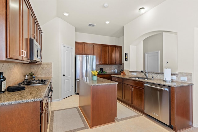 kitchen featuring visible vents, appliances with stainless steel finishes, a sink, a kitchen island, and light stone countertops