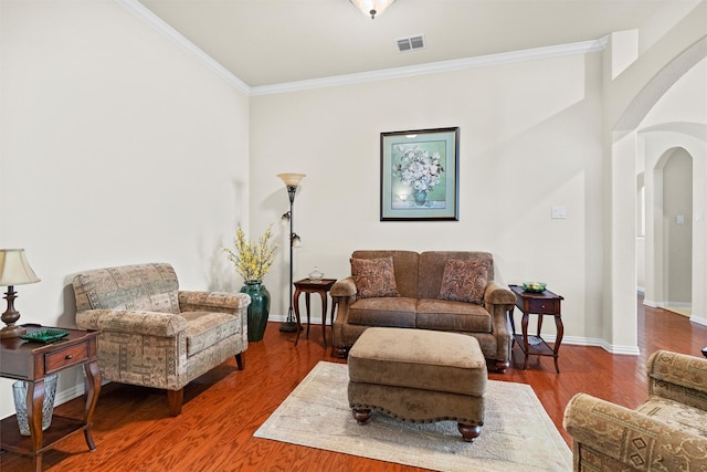 living area featuring arched walkways, wood finished floors, visible vents, baseboards, and crown molding