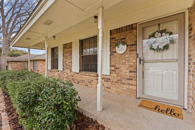 doorway to property featuring covered porch and brick siding