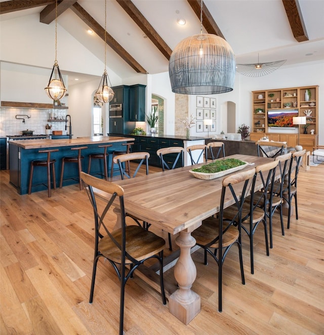 dining space featuring arched walkways, high vaulted ceiling, beamed ceiling, and light wood-type flooring