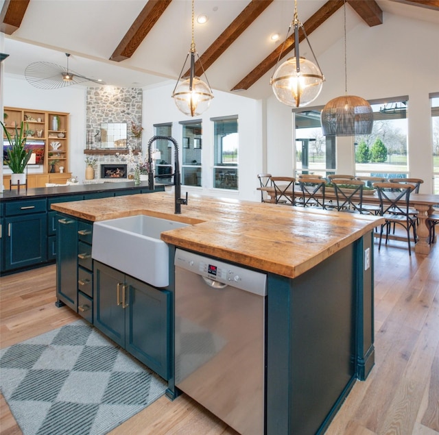 kitchen featuring stainless steel dishwasher, butcher block countertops, a center island with sink, and blue cabinets